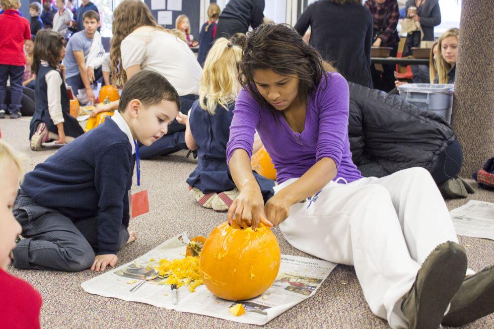 Senior Aria Bryan helps her kindergarten partner carve into his pumpkin. "The children come home and talk about it. It’s a big deal; [seniors] are like stars to them,” Upper School Dean of Students Judy Cummins said.