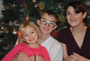 Senior Victoria Guest (far right) poses with younger siblings Cameron Guest (center) and Olivia Campbell (left) in front of their 2013 Christmas tree. “We decorate with silver and frosted glass balls and glittery snowflakes that are purple, pink, turquoise, and green,” Guest said.