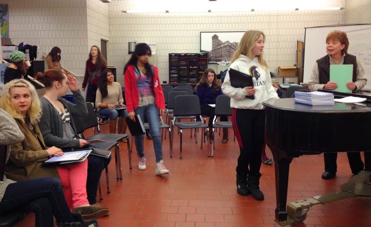 Students file into a morning Summit Singer rehearsal and begin to take their place by section: alto, first soprano, or second soprano. 