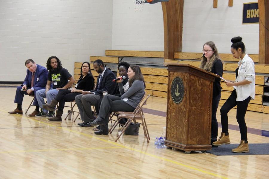 Seniors Evva Parsons and Mansuda Arora introduce the panel of Paul Applebaum, Chris Lollie, Lonna Stevens Hunter, Jaylani Hussein, Ashley Johnson, and Sarah Herder at the MLK assembly.