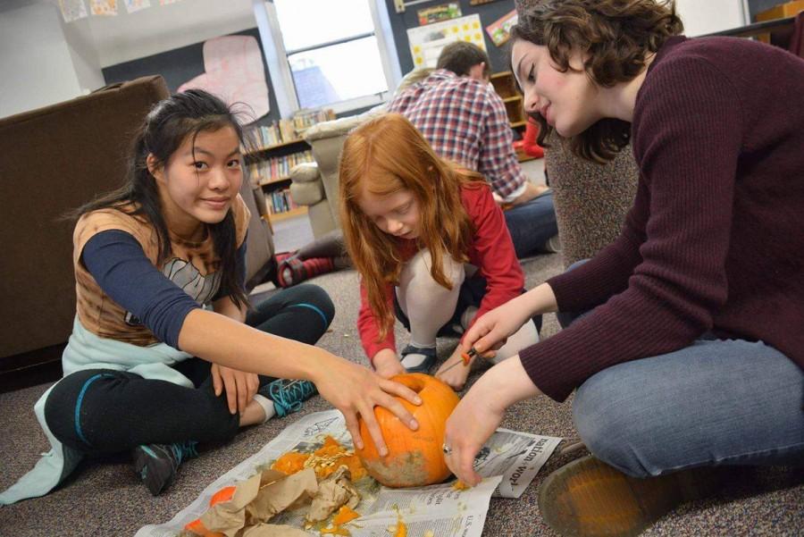 Seniors+Elena+Youngdale+and+Maggie+Vlietstra+work+together+with+their+kindergartner+to+carve+a+pumpkin.