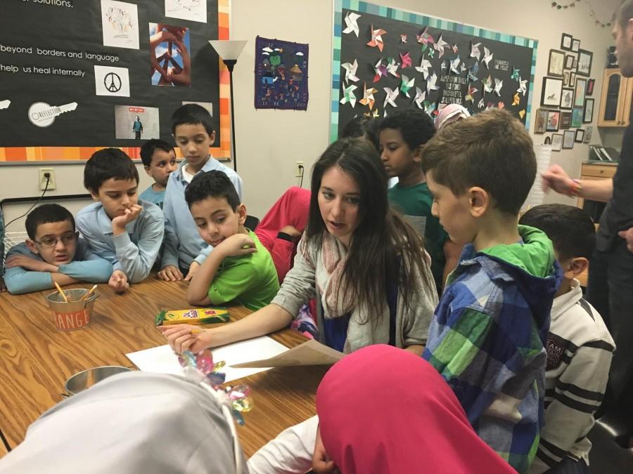 Children gather around their art teacher at Global Academy, one of the locations where SPA students volunteered, watching intently as she teaches them to draw a Quetzal bird from Central America. 