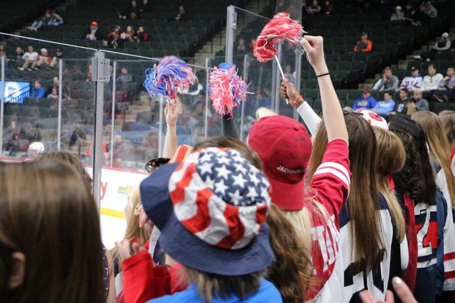 Fans from SPA and Visitation wave red, white, and blue pom-poms in the air to show their support for the SPU Hockey team. 