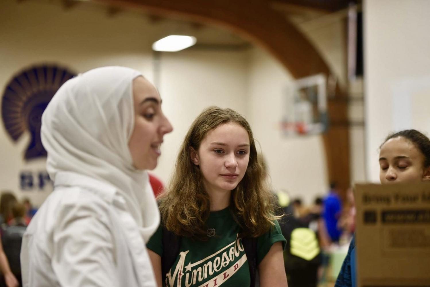 Senior and president of Muslim Student Alliance Iya Abdulkarim shows 9th grader Margot Bergner the MSA poster. 