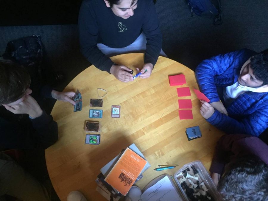 Seniors Ned Laird-Raylor, Turab Naqvi and Arib Rahman play Yu-Gi-Oh! cards in the senior lounge as  spectators look on. Laird-Raylor relies on three things for his competitions:“First, building the deck: what cards are in the deck. Second is how I play with those cards, because a good player with a bad deck can still beat a bad player with a good deck. Lastly: the belief of the heart of the cards.”