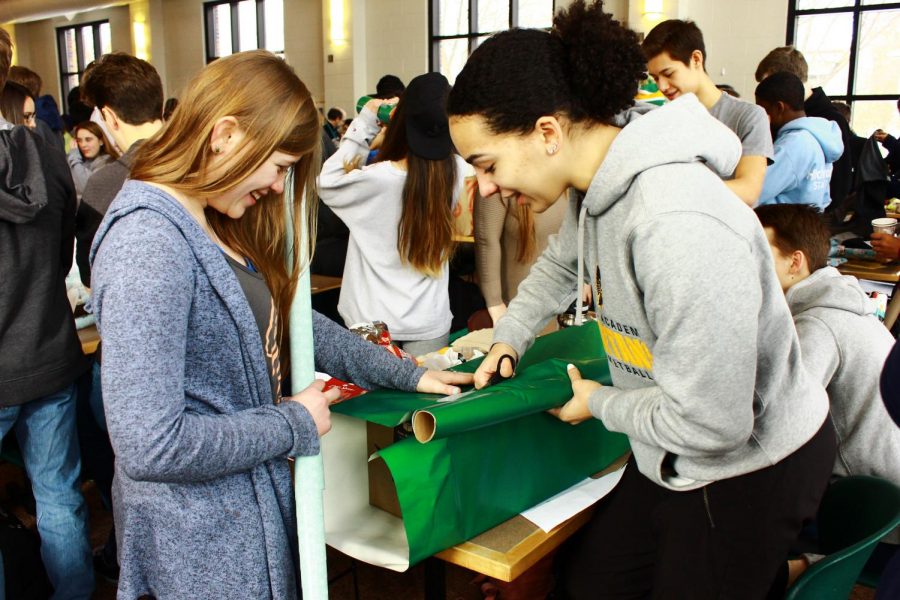 Seniors Dorienne Hoven and Izzy Denny laugh as they wrap a present for a family in need. 