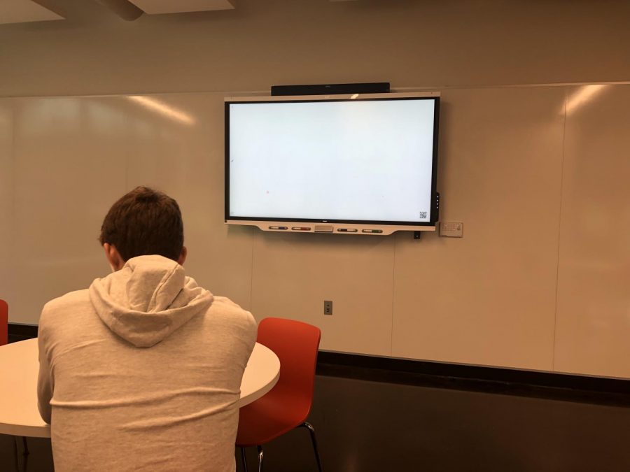 Senior Will Christakos studies in the Schilling Center in front of an unused smartboard.