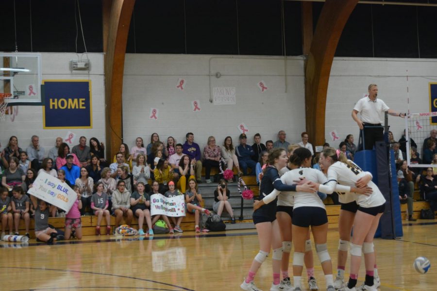 The volleyball team meets up with one another after a point while the junior Spartans cheer them on. 