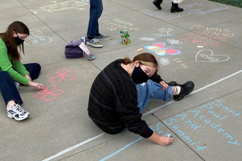 Seniors Isobel Alm and Hannah Lorenz-Meyer color the pavement with flowers and SPA logos.  