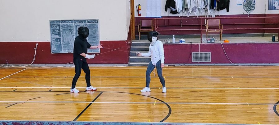 Fencing coach Sasha guides a student by holding the Foil weapon to demonstrate a movement.