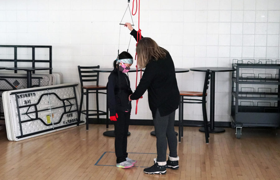 Coach Debbie Warne-Jacobsen readies a harness for Lydia Chen, in order to lift the skater up into the air to practice spinning.