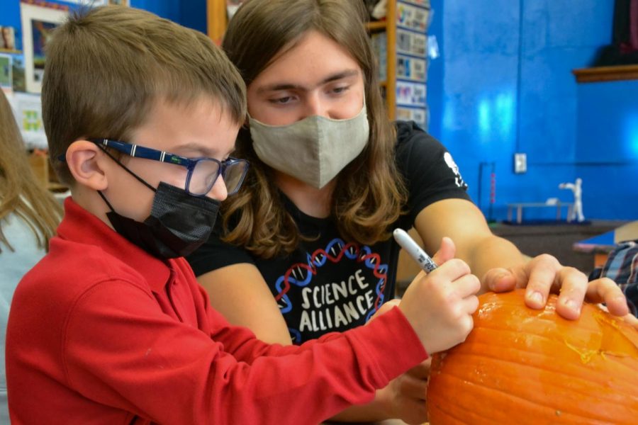 Senior Will Sedo helps a kindergartener draw a face on his pumpkin before they begin carving the pumpkin out. Sedo noted he really enjoyed, helping [the lower school student]s bring their pumpkin carving ideas to life.  
