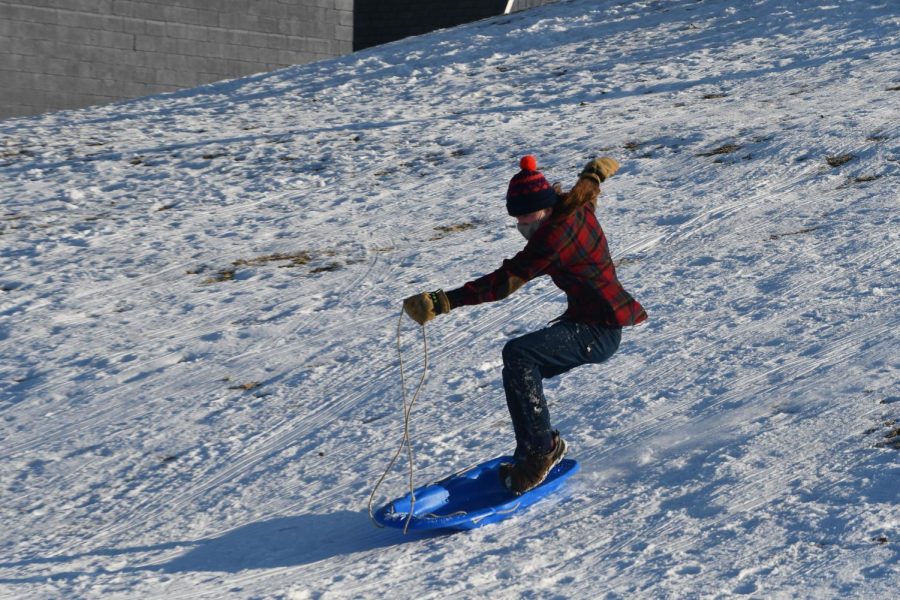 SURFING THE SNOW. Senior Will Sedo balances on a sled as he goes down the hill. Sedo said, "It was really great to get out sledding with Outdoors Club on Thursday. We’ve had sledding parties like this in past years, but this was by far the biggest crowd we’ve ever had. It was fantastic to see everybody out there, and the hot chocolate was a treat."