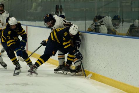 Freshman Ethan Peltier forces a Breck player off of the puck as junior captain George Peltier scoops it up.
