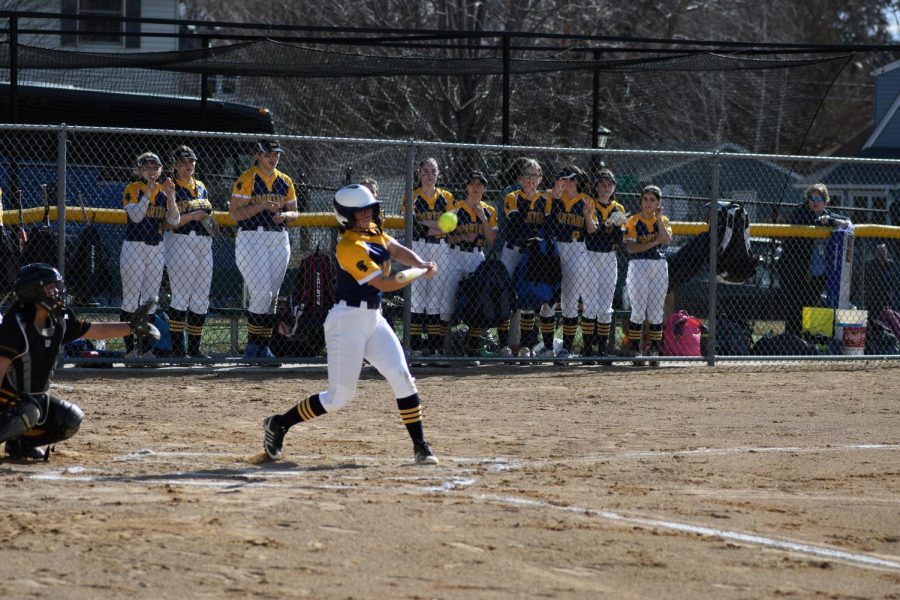 SWING BATTER. Captain Rowan Benz swings at a pitch with her team watching from the dugout. Benz is known most for her pitching, and captain Greta Magnuson said, Benz will add a new level to the game.”