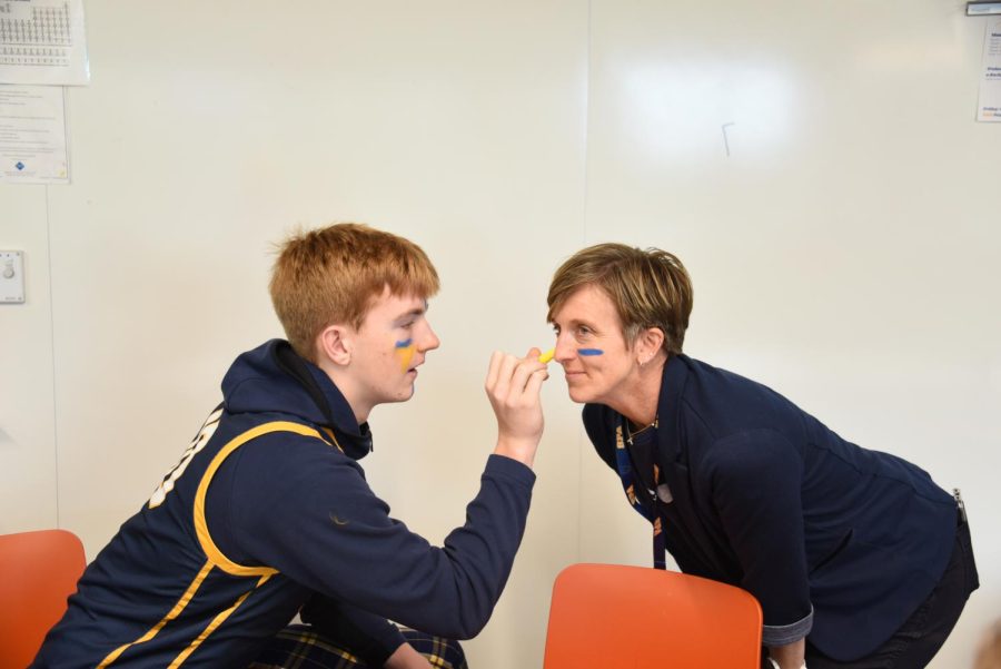 FACE PAINT FUN. Junior Tysen Hayes gives Dean of Students Stacy Tepp a festive makeover with blue and gold face paint. Both students and faculty are truly in the Homecoming spirit.