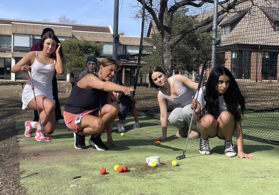 PREDICTIVE POINTING: Head coach Angie Kritta points out the bumps in the turf that the players need to watch out for during their afterschool practice on Apr.11. Team members listened intently while Kritta explained how to use the unevenness of the ground to their advantage. “We were looking for the angle of the putt,” Freshman Millie Farrington explained.