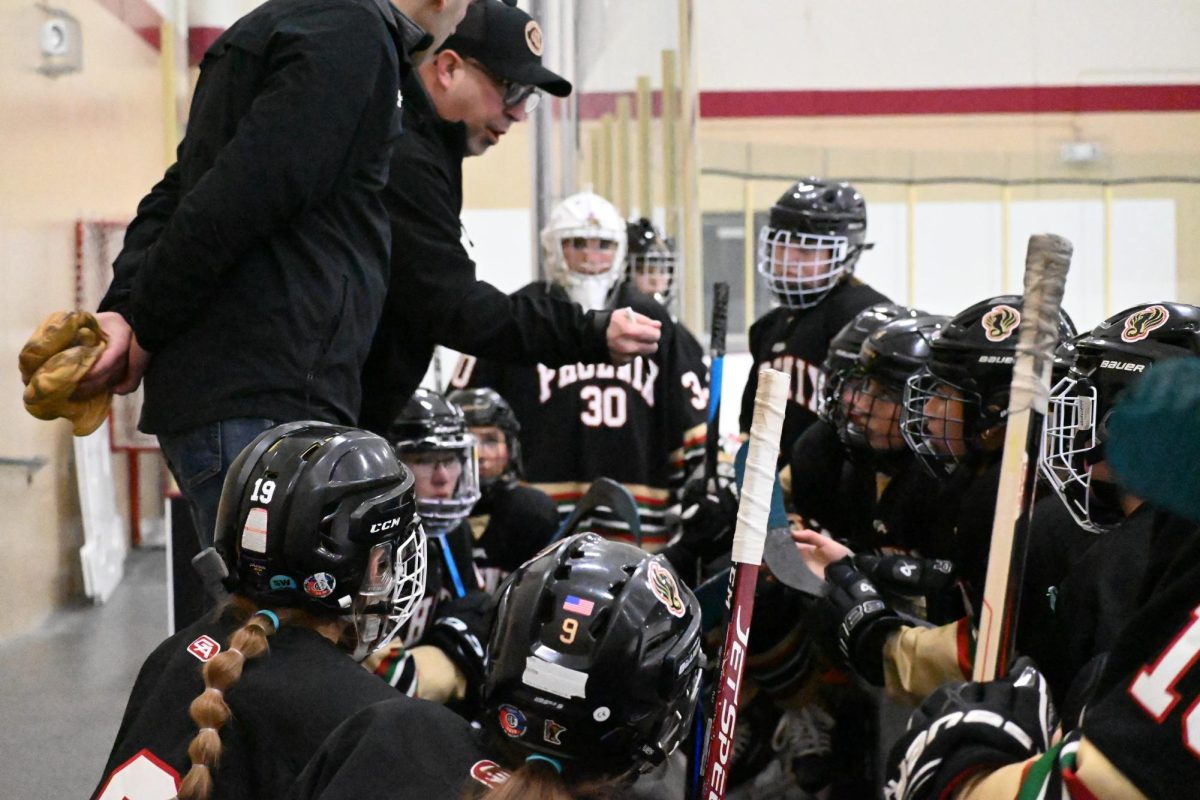 UPING THE ANTE. Coach Ziegler spoke about game plans with the team as they came off the rink. Everyone gathered around as the decision to take goalie Millie Farrington out of the game in order to increase their chances of scoring was made. “It was very stressful when we pulled Millie, but I think there was nothing to lose, so I feel like it made me play a little better, said center Ella Bond.