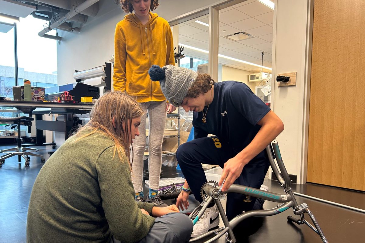 TEAM EFFORT. Club leader Bennett Sauer and club members Ava Doody and Leif Rush sit together in the design lab as Sauer work at deconstructing one of the mainframes for the go-kart. Doody and Rush watch Sauer exchange tools to work on the frame as they discuss what to do next in the creation process.