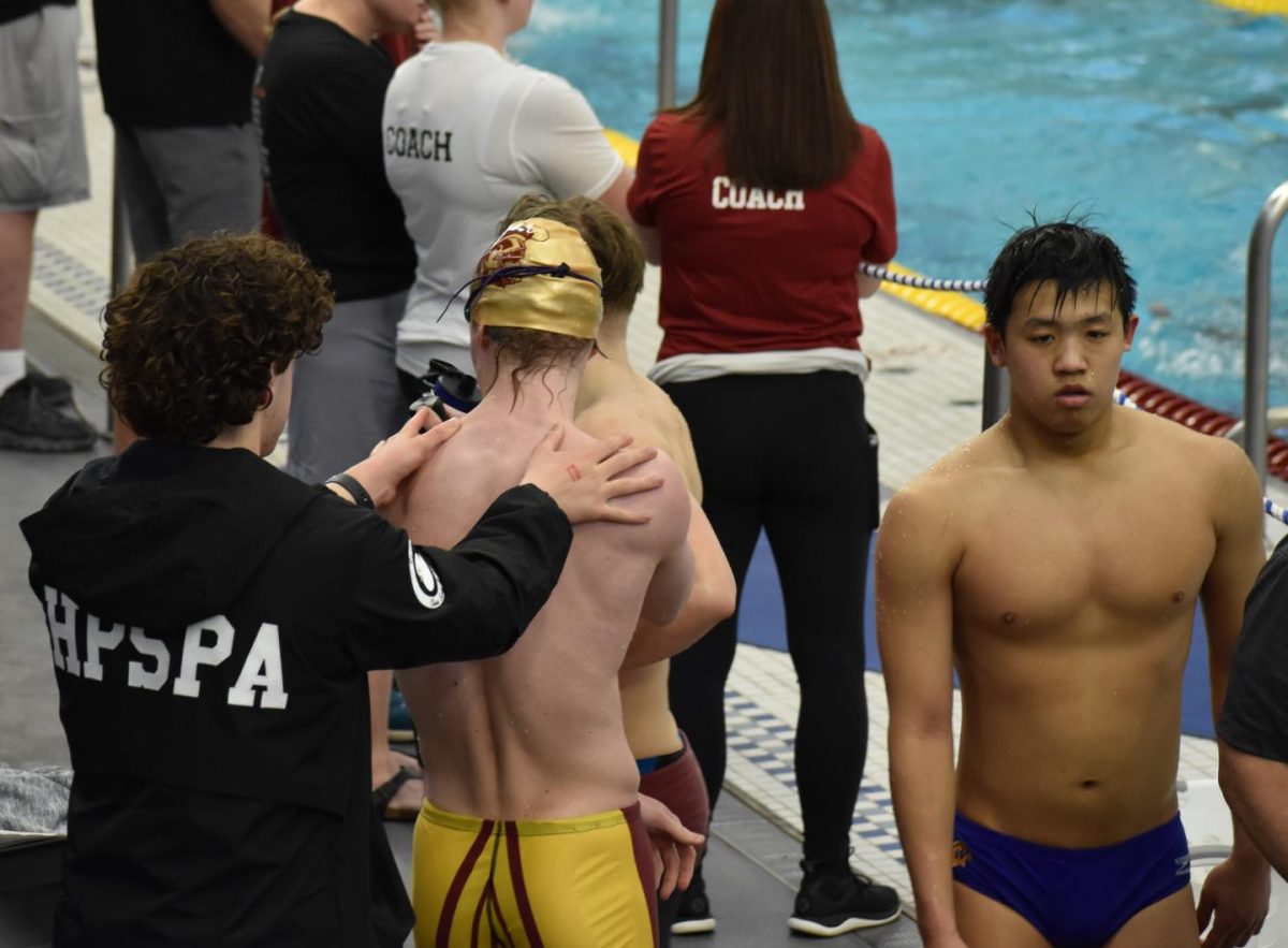 TEAM SUPPORT. Junior Finn Cox helps senior Connor Overgaad prepare his body for the relay. A few of the quartets teammates attended the meet to support the swimmers.