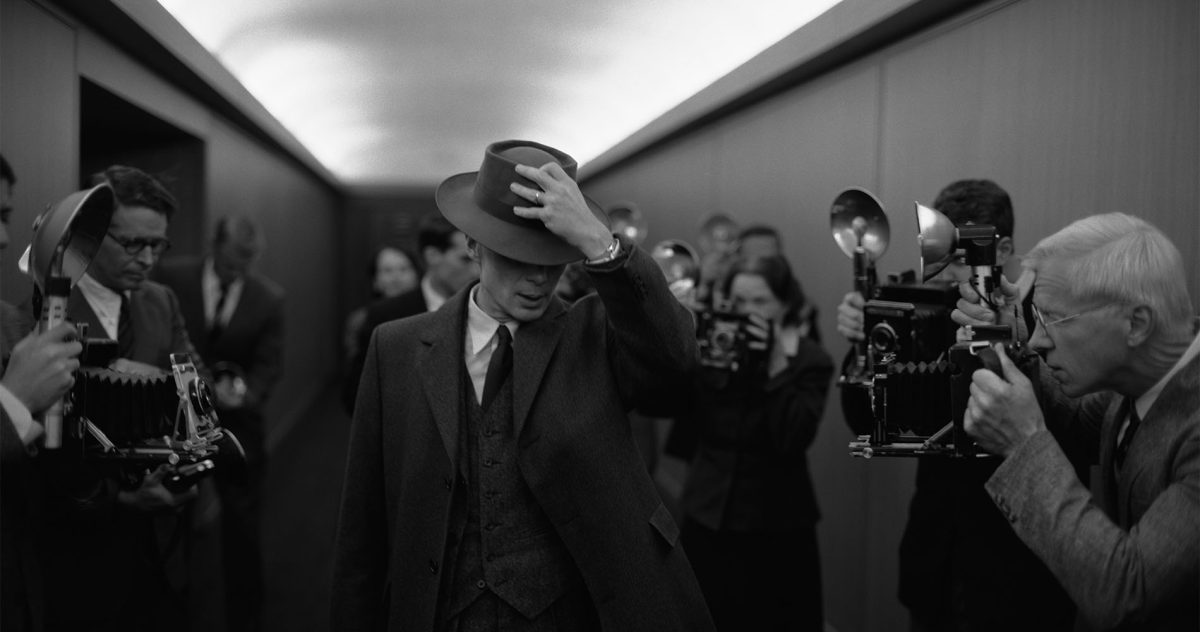 STOIC AND MYSTERIOUS. Dr. J. Robert Oppenheimer (Cillian Murphy) pushes his hat over his face in an intense monochromatic scene.