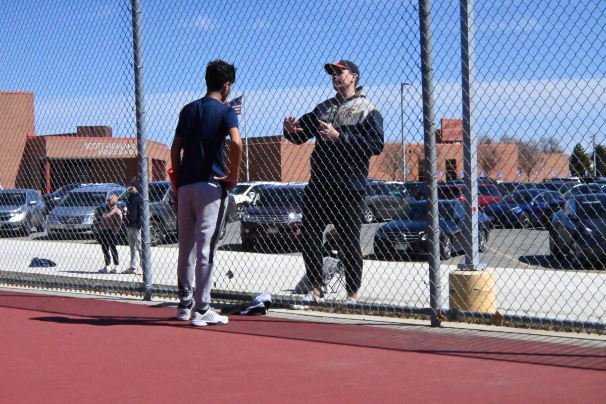 THROUGH THE FENCE. Coach Luke Elifson speaks to freshman Zahir Hassan through the fence after his match with some pointers. "Reinforcing and encouraging each other to do the right things within it. [...] Attack shot but encourage each other to go for the right ball more, whether you fail or succeed," said coach Elifson.