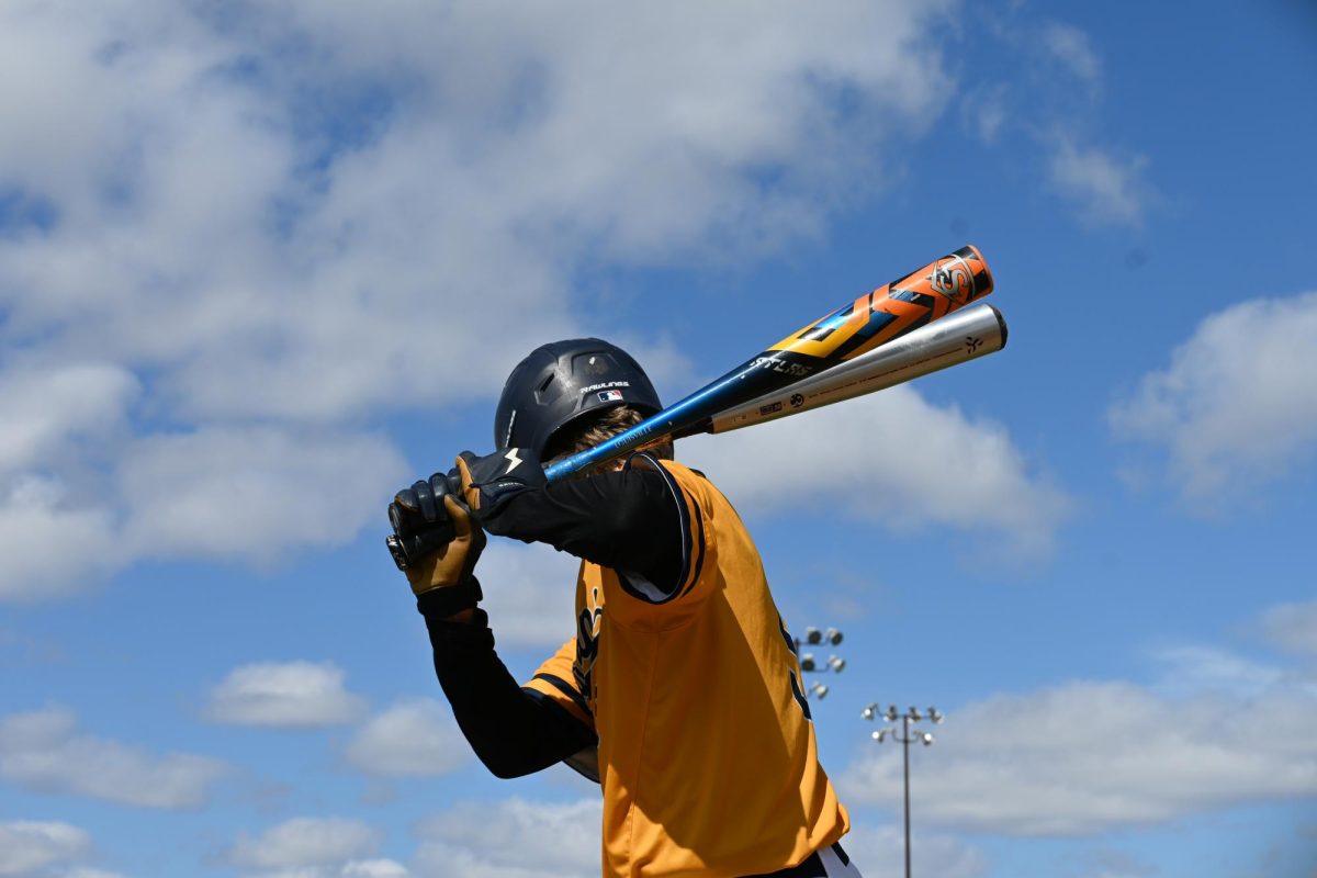 PRACTICE SWINGS. Freshman John Grimsrud takes some swings with two bats while on deck, waiting for his turn at the plate during the game against Eagle Ridge Academy on Apr. 20. Grimsruds teammate James Welsh said, I think were going to start winning some games here. Weve cleaned up our fielding, and if we can fix our hitting, were gonna be a really good team.