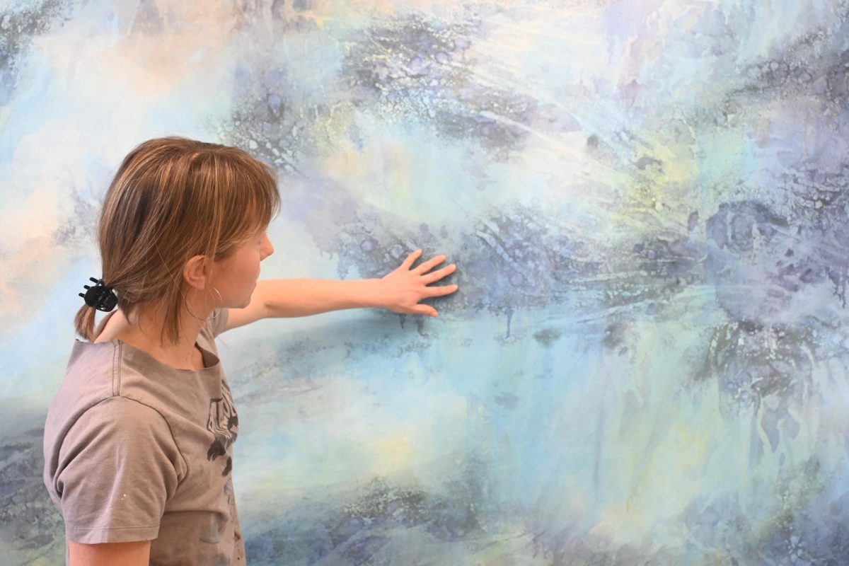 PLAYING WITH TEXTURE. Hejny demonstrates the rough texture on her 18-foot-tall commissioned painting from the salt added to the paint. 