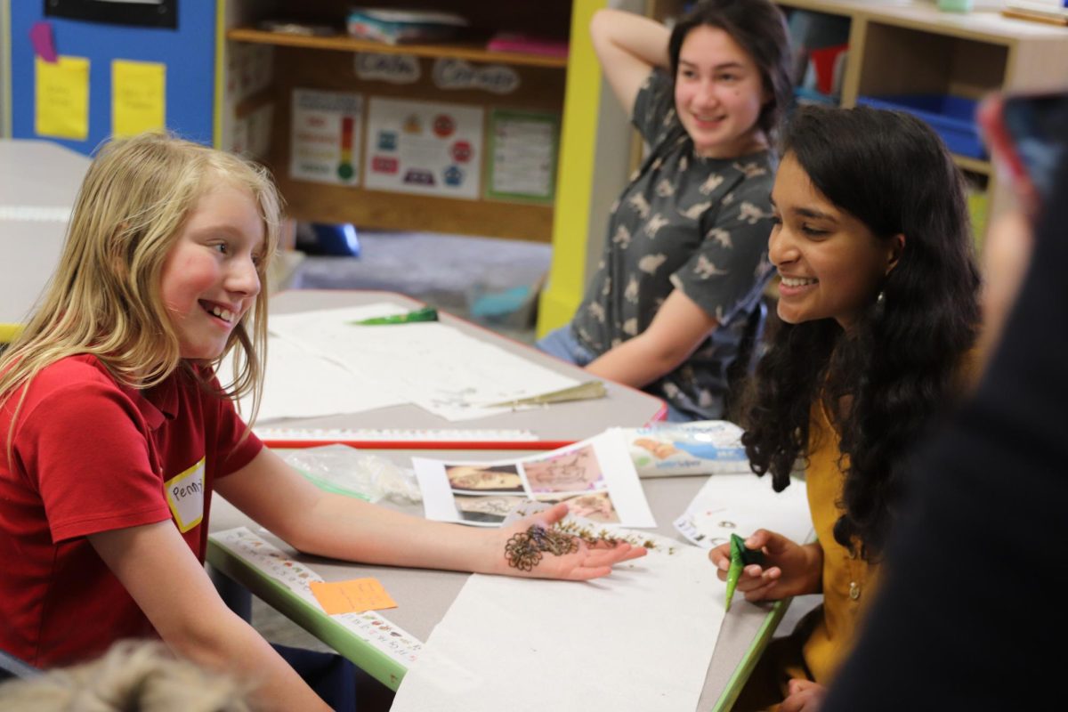 SMILES SHARED. Freshman Nabeeha Qadri applies henna to a Lower School student’s hand. Qadri’s henna was one of many stations that displayed various cultures at the Lower School Family Discovery Night in April 2023. Photo: SPA Smug Mug 2022-2023 Archive.