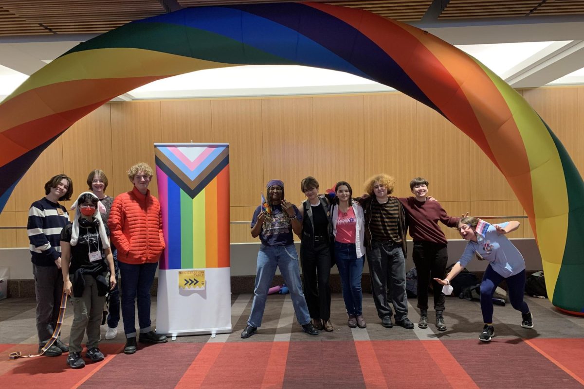 Q-QUEST. Students participating in Q-Quest pose for a group photo under a rainbow arch (Photo submitted by Jack Bettenburg).
