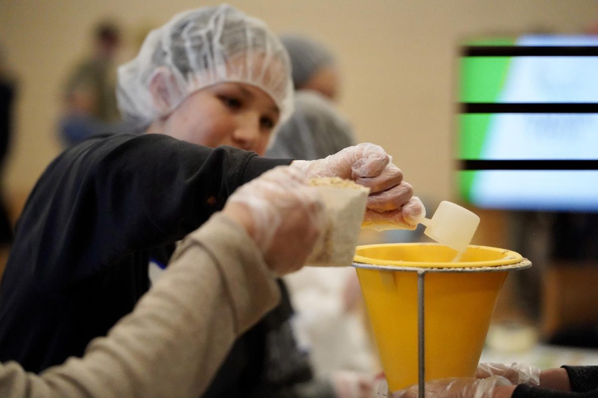 SERVING WITH CARE. Volunteers wear gloves and hair nets while scooping and packing meals up.
