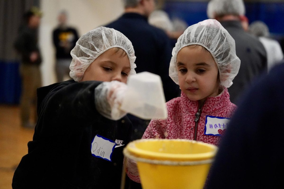 OATS, CINNAMON, SUGAR, OATS. Students, parents, and faculty work together to scoop three ingredients into the yellow funnel to prepare meals for those in need.