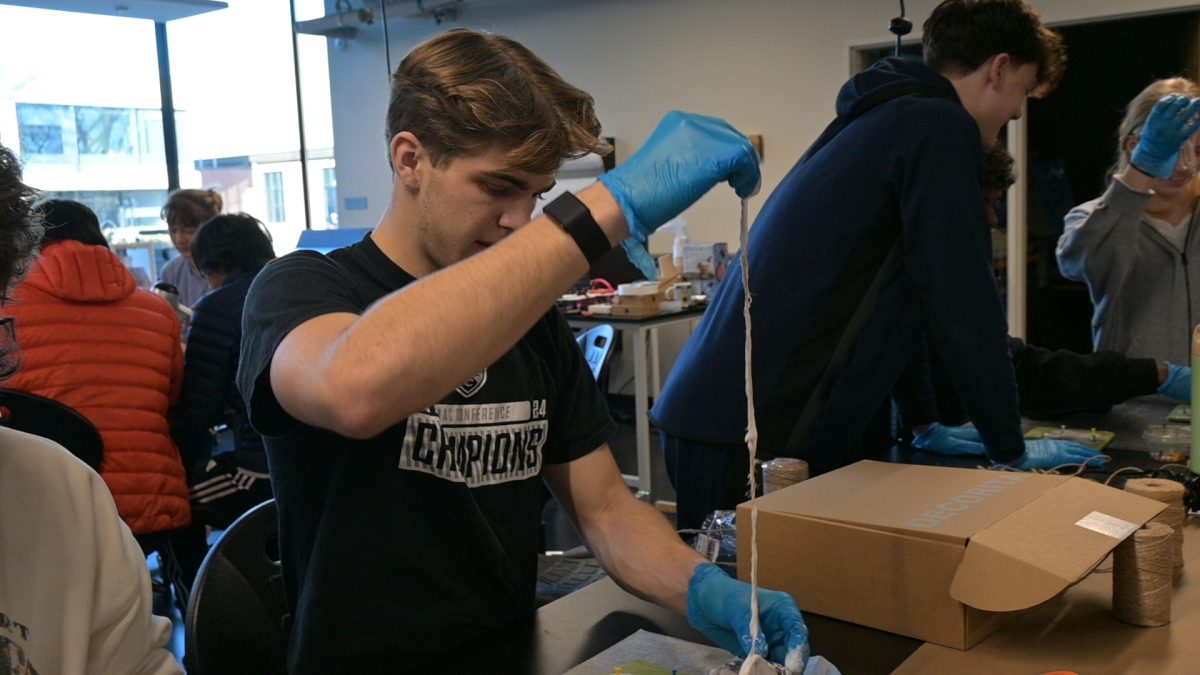 STICKY STUFF. Senior Ethan Peltier pulls twine out of a cup of glue.