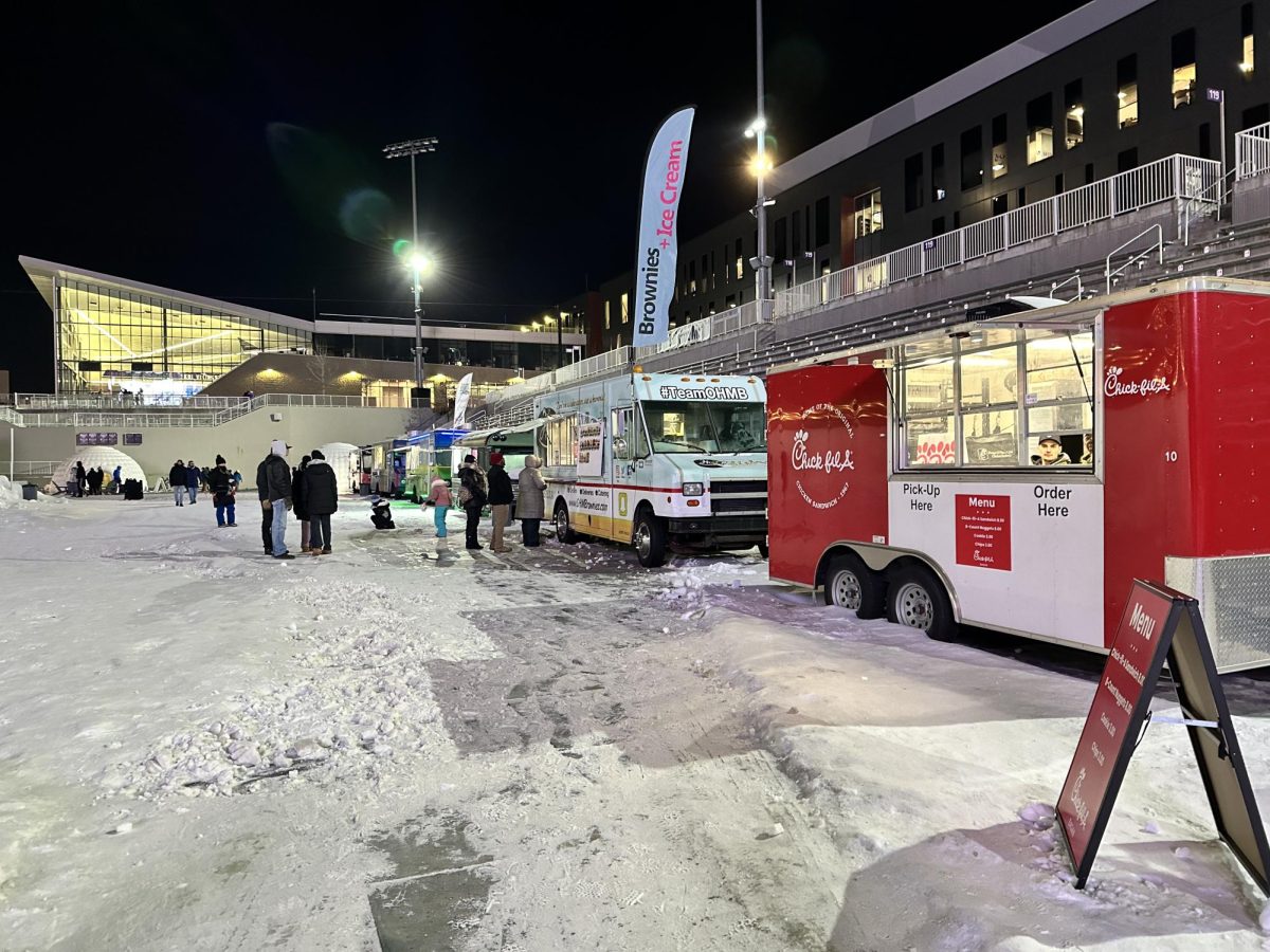 FOOD TRUCK FRENZY. A variety of food trucks are parked in a row along the edge of the stadium. 