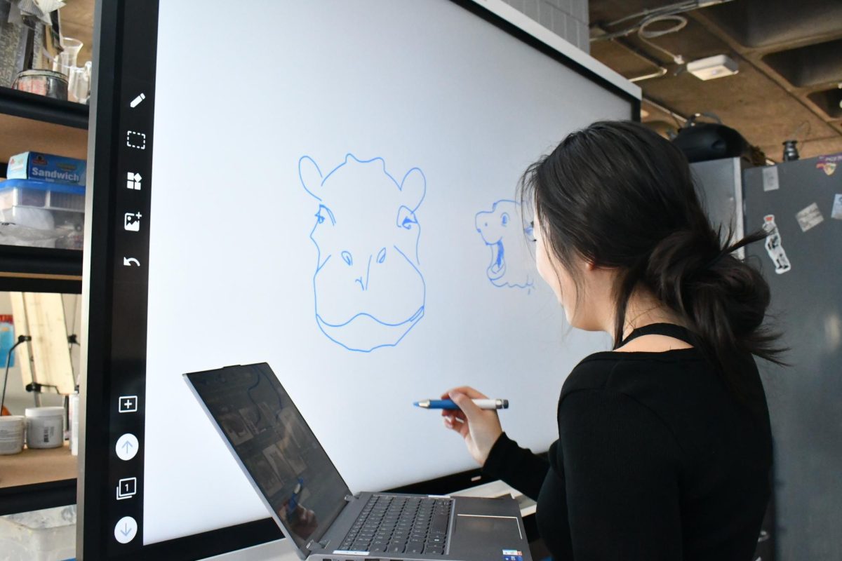 HIPPO TALK ON THE BIG SCREEN. Junior Amanda Hsu draws hippo faces on the smart board while the rest of the Peterson advisees prepare to film.
