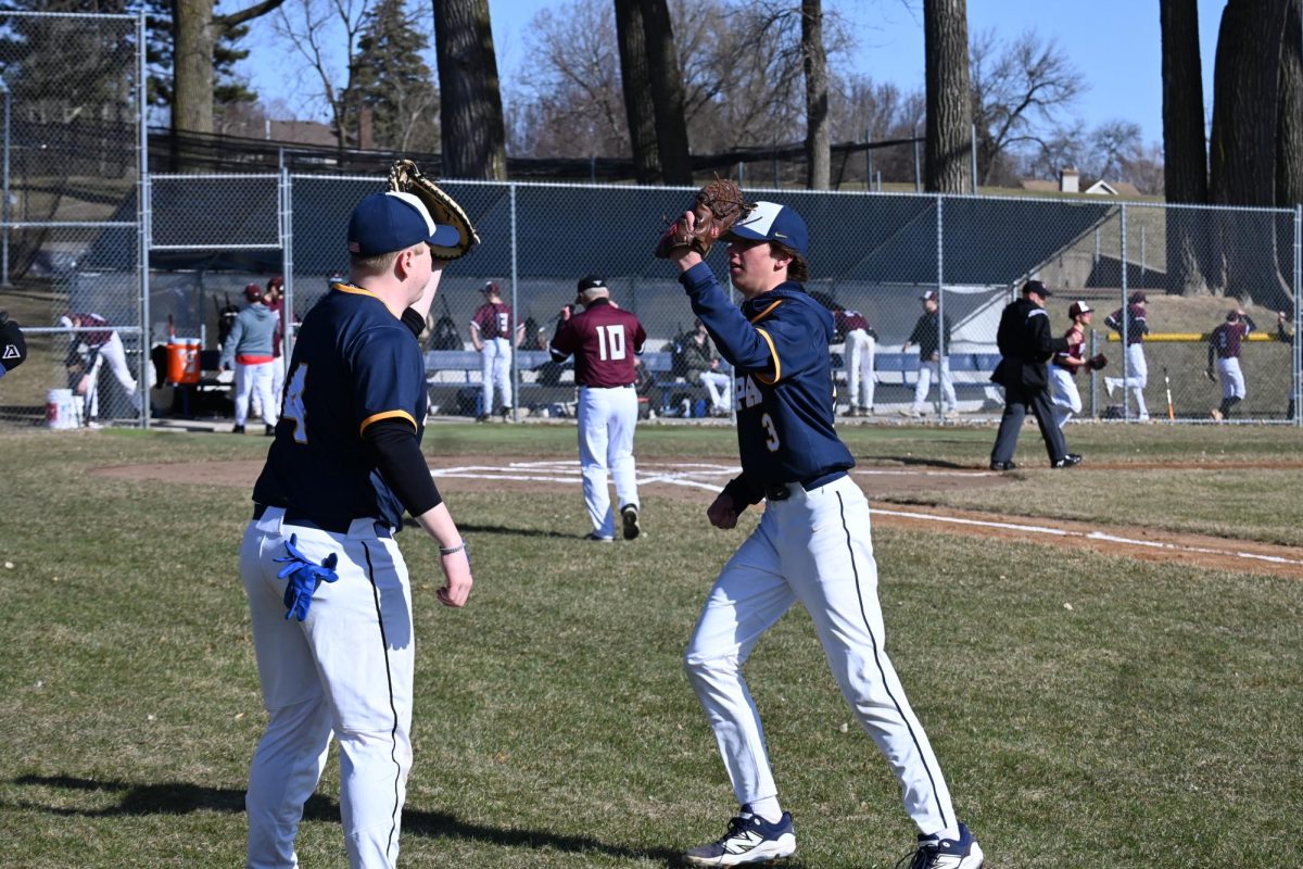 HIGH GLOVE. Junior Peter Ostrem high fives sophomore Charlie Zakaib. Ostrem brought a lot of energy to the team and cheered loudly for every teammate up to bat.