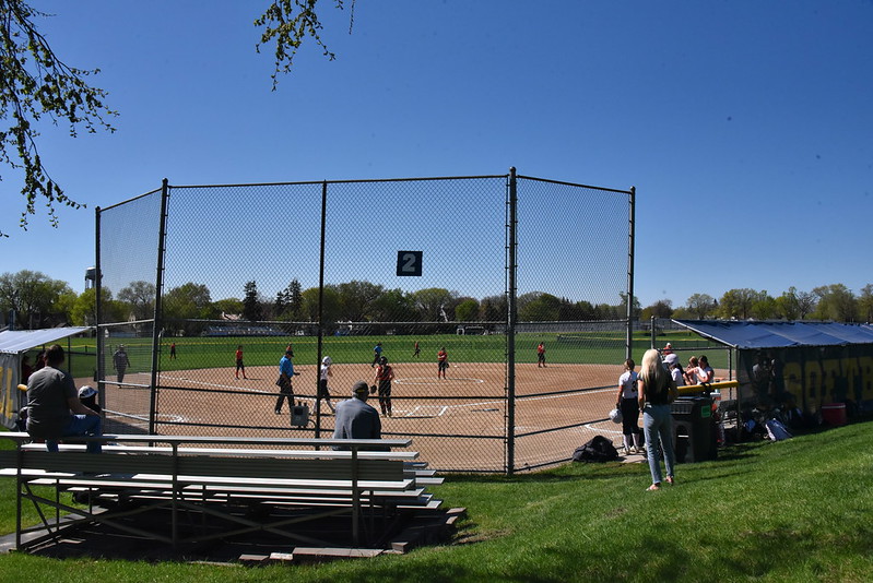 FULL STANDS: The Redhawks take place on the field to warm up before their first game. Breck, Minnehaha, and SPA families would soon fill the bleachers near the fence. Others who came after the bleachers were full sat on the hill behind the field or off to the side of the Redhawks dugout. 
