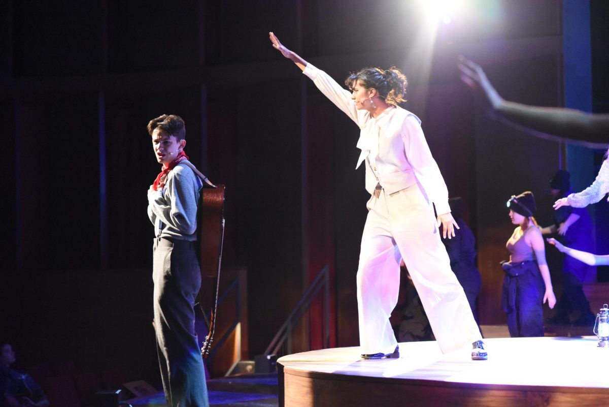 A SONG TO FIX WHAT'S WRONG. Missus Hermes (Aarushi Bahadur) stands over Orpheus (Coda Wilson) paralleling how she guides him throughout the musical. 