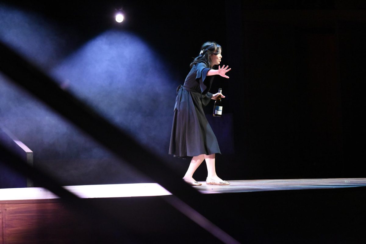 STORYTELLING. Persephone (Ellie Putaski) now sports a black dress to signify she resides in the underworld. She is still pictured with alcohol, showing the pervasiveness of her and Hades's fracturing relationship. 