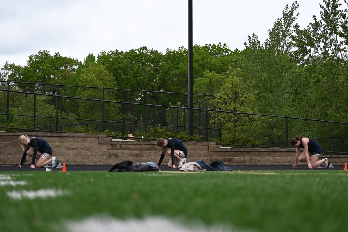 ON YOUR MARKS. Ninth-grader Lucy Byrnes, junior Elizabeth Tuttle and junior Clare Ryan Bradley (left to right) settle into their blocks for their 200 meter heat.
