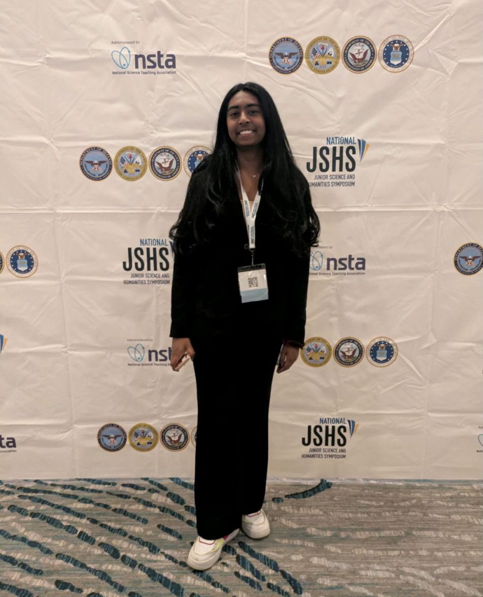 ALL SMILES FOR SCIENCE. Junior Shefali Meagher poses in front of a JSHS banner in her presentation attire. (Photo submitted by Shefali Meagher)