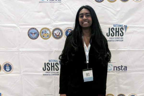 ALL SMILES FOR SCIENCE. Junior Shefali Meagher poses in front of a JSHS banner in her presentation attire. (Photo submitted by Shefali Meagher)