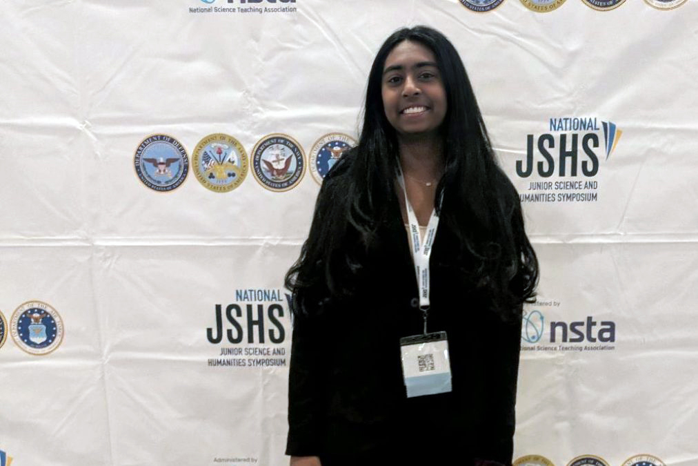 ALL SMILES FOR SCIENCE. Junior Shefali Meagher poses in front of a JSHS banner in her presentation attire. (Photo submitted by Shefali Meagher)