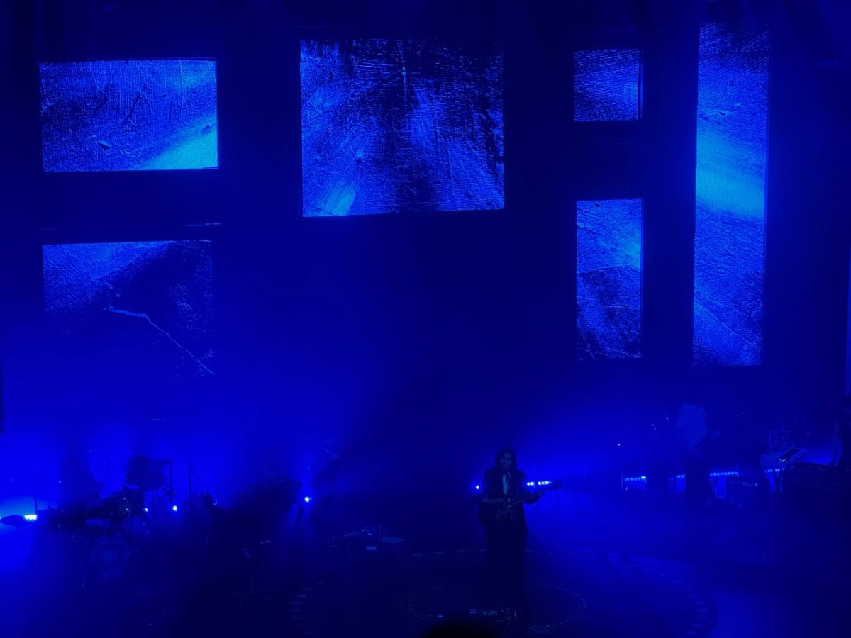 STUDY IN BLUE. The transitioning artwork behind Dacus is a strengthening supplement to the music. At one point, six individual portraits, each depicting a different member of the band, project brightly in the dim background.