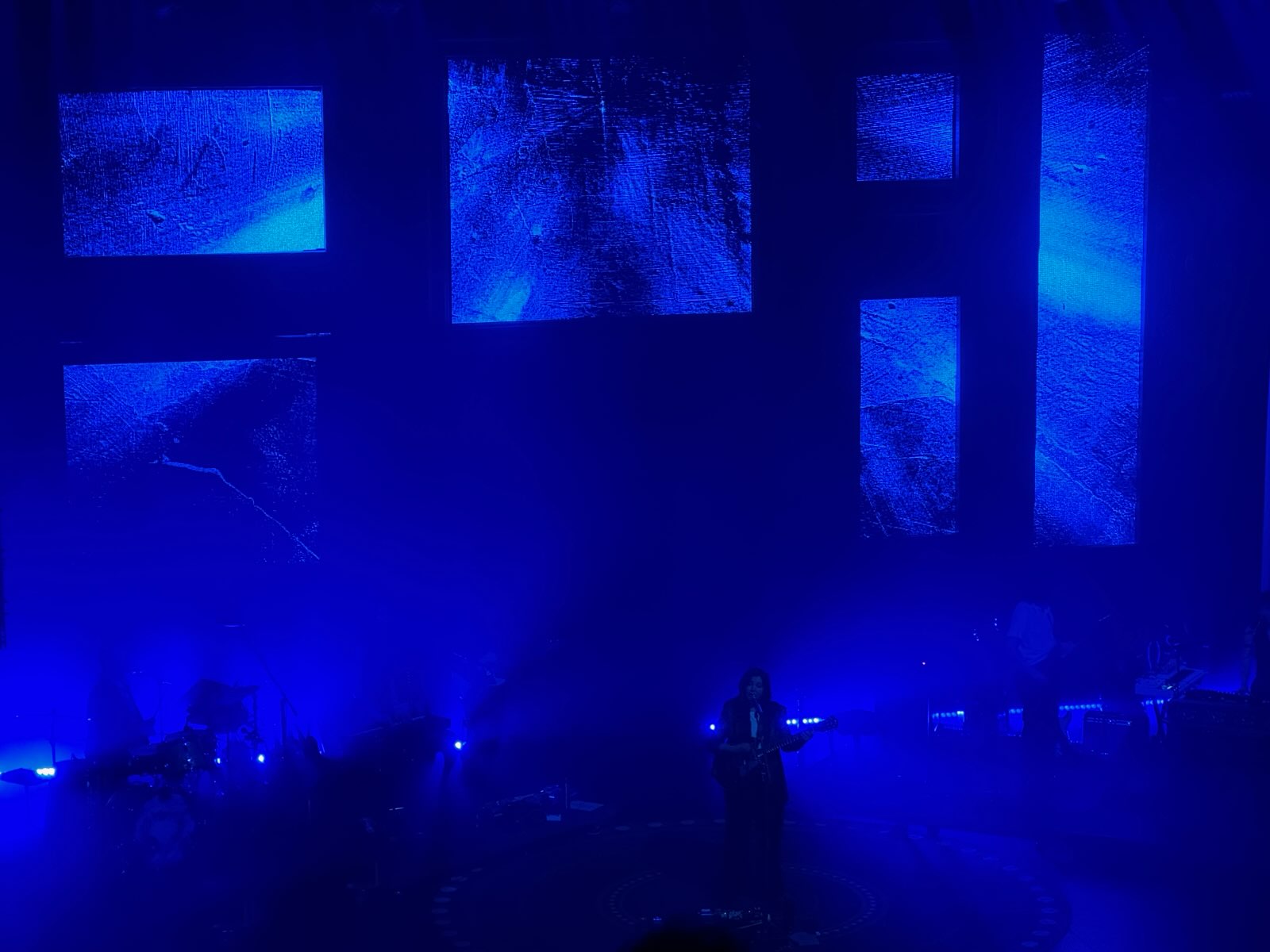 STUDY IN BLUE. The transitioning artwork behind Dacus is a strengthening supplement to the music. At one point, six individual portraits, each depicting a different member of the band, project brightly in the dim background.