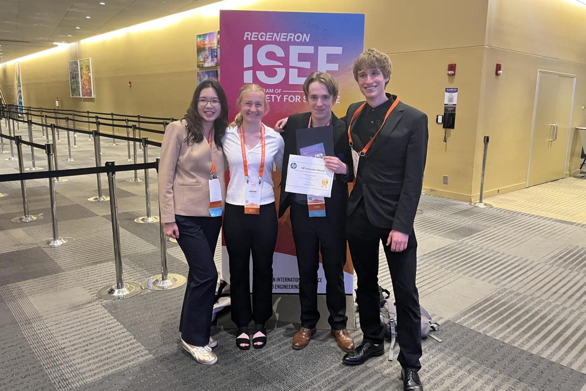 IN IT TO WIN IT. (From left to right) Senior Deling Chen, juniors Maren Overgaard, Huxley Westemeier and Evan Morris pose in front of a Regeneron ISEF poster. 