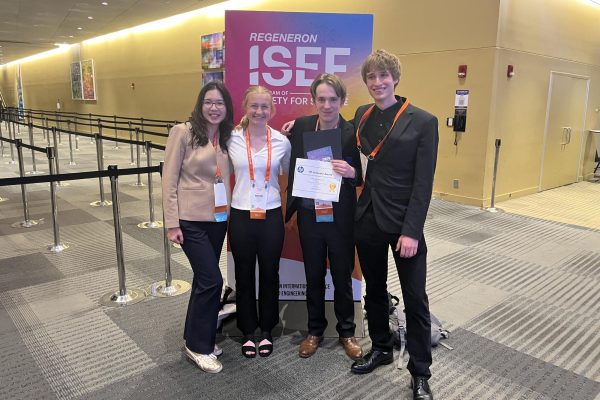 IN IT TO WIN IT. (From left to right) Senior Deling Chen, juniors Maren Overgaard, Huxley Westemeier and Evan Morris pose in front of a Regeneron ISEF poster. 