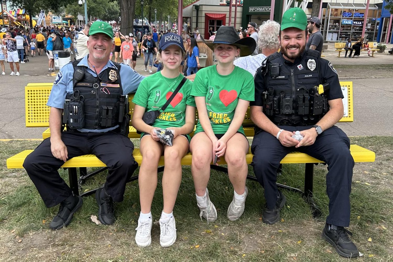 IN A PICKLE? Junior Avital Coleman, alongside coworker Lila Montgomery (also a junior), poses with police officers. Coleman and Montgomery are both working their second year at “The Perfect Pickle,” where they make deep-fried pickles and hang out around the fair before and after shifts. “It's definitely a really entertaining job and very high pace; it's pretty chaotic,” Coleman said. “I work at the trailer, which is really busy because it's right by the midway. It's definitely been a bit overwhelming, just considering how much homework I have, but I really enjoy it, so I make it work.” (Submitted Photo: Avital Coleman)
