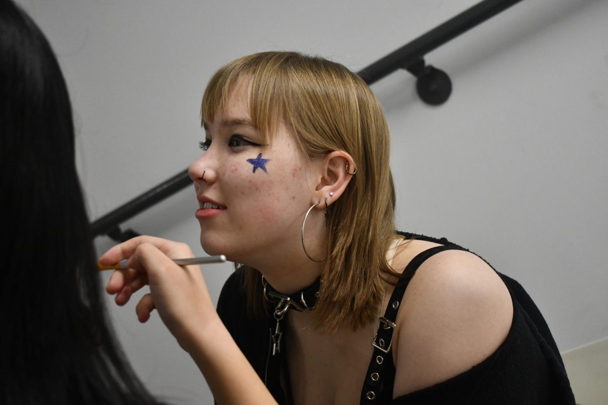ROCKSTAR. Purple Weekend's Taryn Karasti does her makeup before soundcheck. Senior Carys Hsiung paints a star on Karasti's cheek.