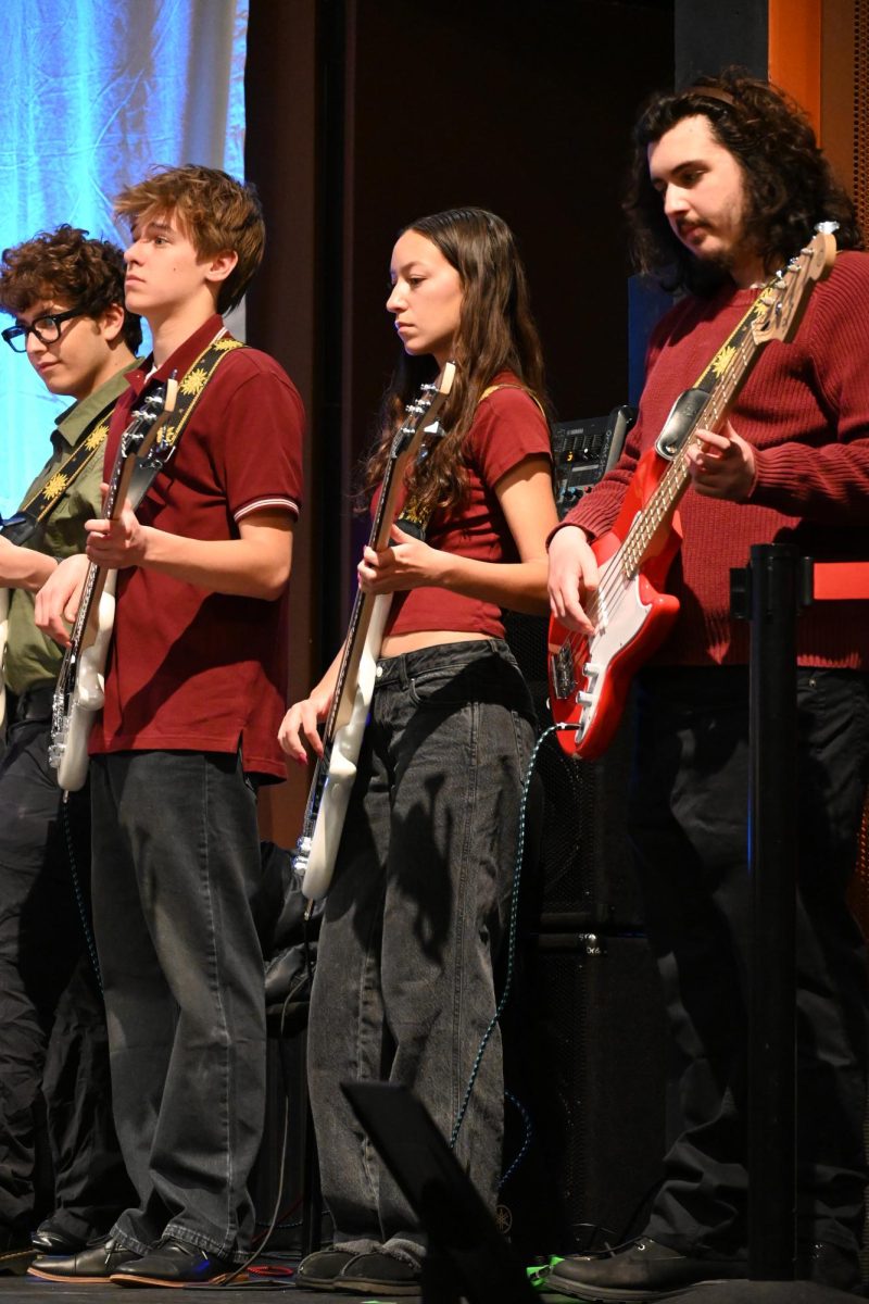 SENIORS IN RED. Seniors Josh Melchert, Sonia Kharbanda and Johann DeVriese pick at the strings of their electric basses for "Skyfall."
